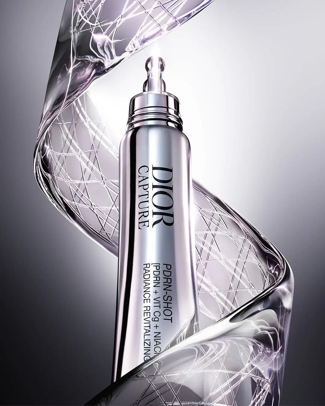 Silver Dior Capture PDRN-Shot tube with pearlescent liquid ribbon swirling around it on a gradient grey backdrop