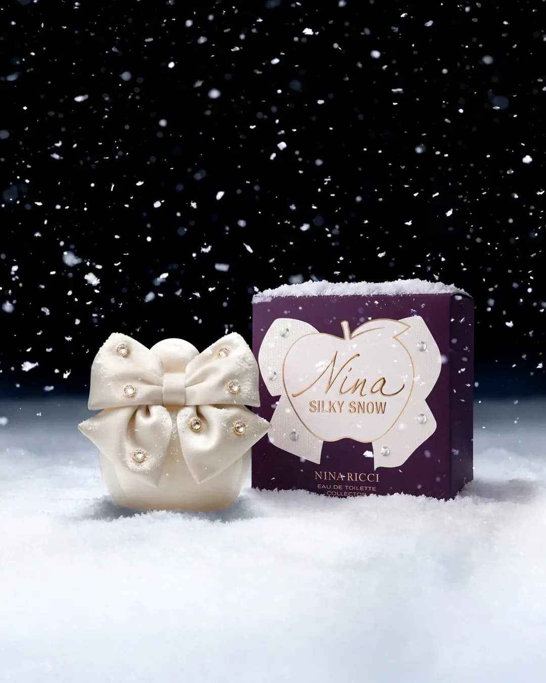 Cream bow-topped bottle beside a purple box with a white apple and bow reading Nina Silky Snow, set in snow