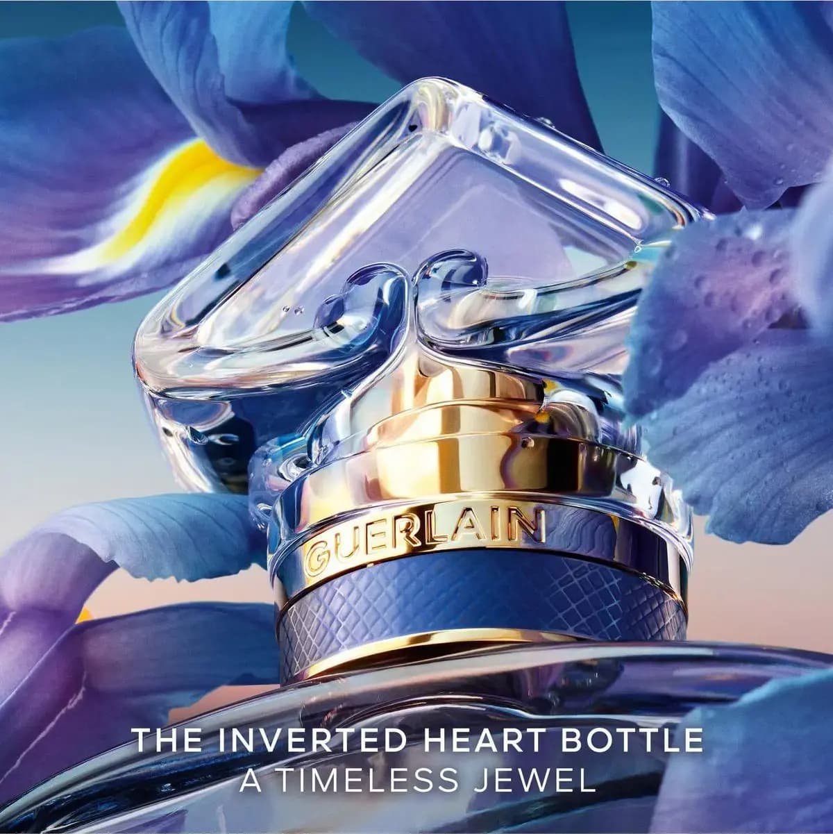 Close-up of the clear heart stopper and gold Guerlain collar with textured blue band, captioned the inverted heart bottle.