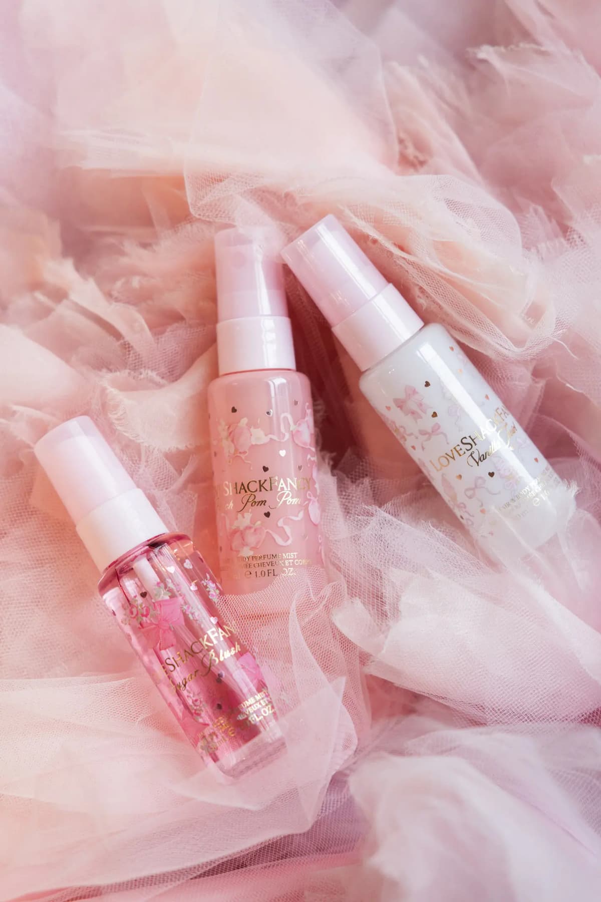 Sugar Blush, Peach Pom Pom and Vanilla Twirl mini mists with pink caps lying on ruffled blush-pink tulle