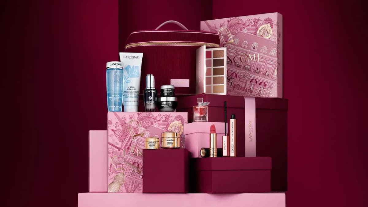Burgundy display showing Lancôme Holiday Beauty Box contents staged on pink and red gift boxes against a deep red backdrop.