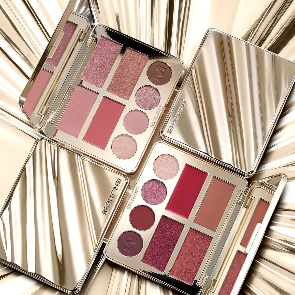 Two open gold Morphe palettes in rosy pink and berry tones laid on a shiny gold metallic backdrop