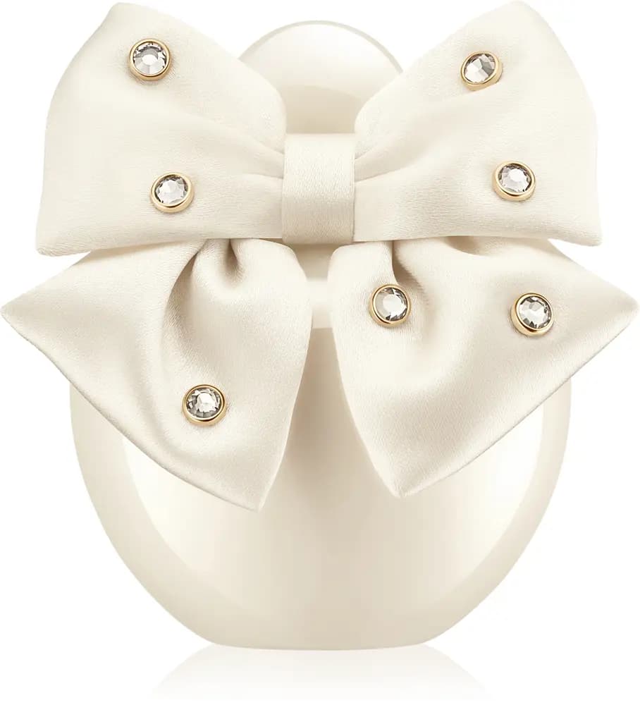 Rounded pearly cream bottle wrapped in a satin bow studded with gold-set crystals on a white background