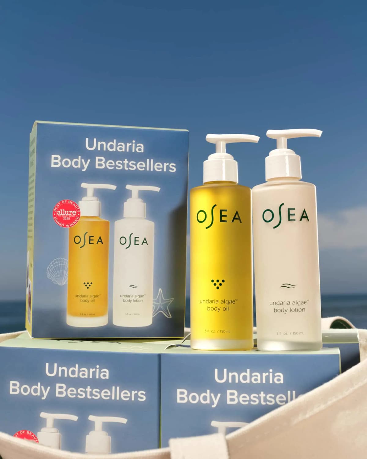 Stacked blue Undaria Body Bestsellers boxes with the body oil and lotion bottles against a blue sky and ocean