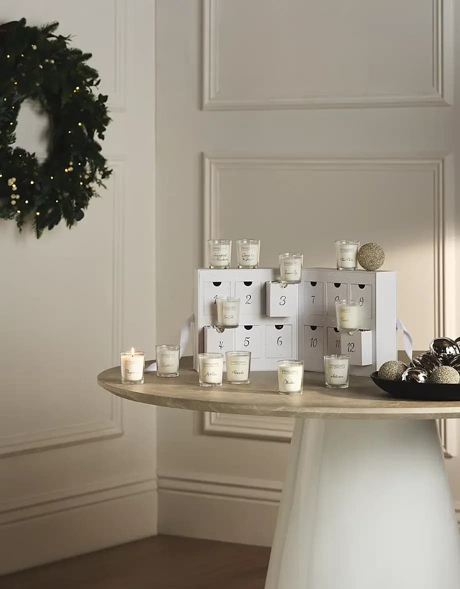 White 12-drawer candle box on a marble table with votives, one lit, beside a lit wreath and silver baubles
