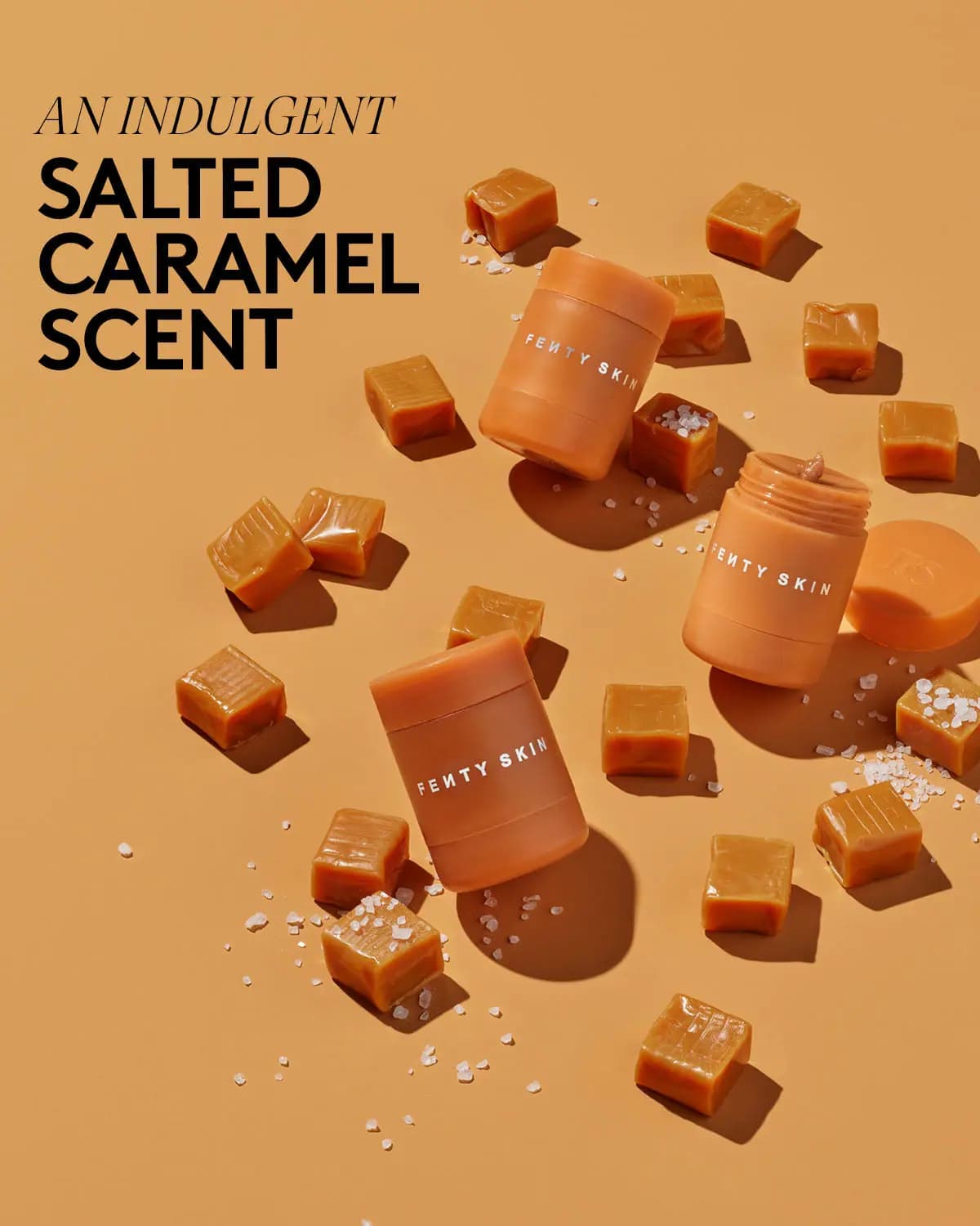 Three peach Fenty Skin jars scattered with caramel cubes and salt flakes on orange backdrop