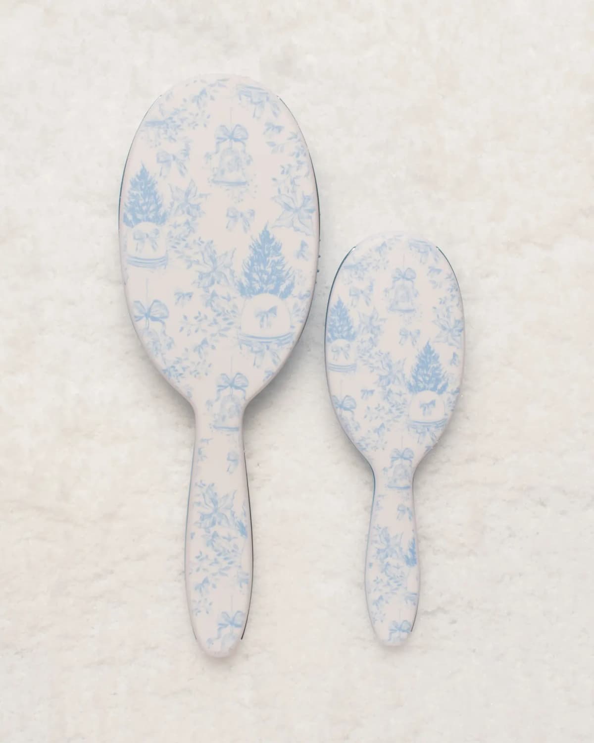 Backs of both FRAMAR brushes showing pale-blue winter toile print of Christmas trees, bells and bows on snow