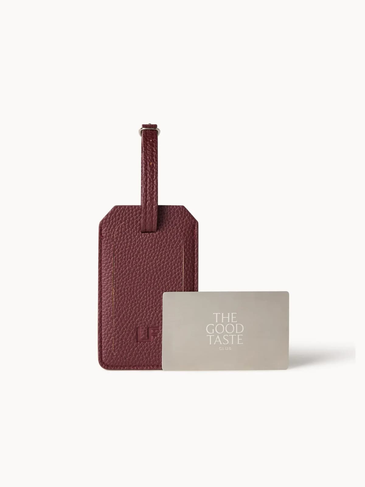 Burgundy pebbled LF luggage tag beside a brushed metal The Good Taste Club card