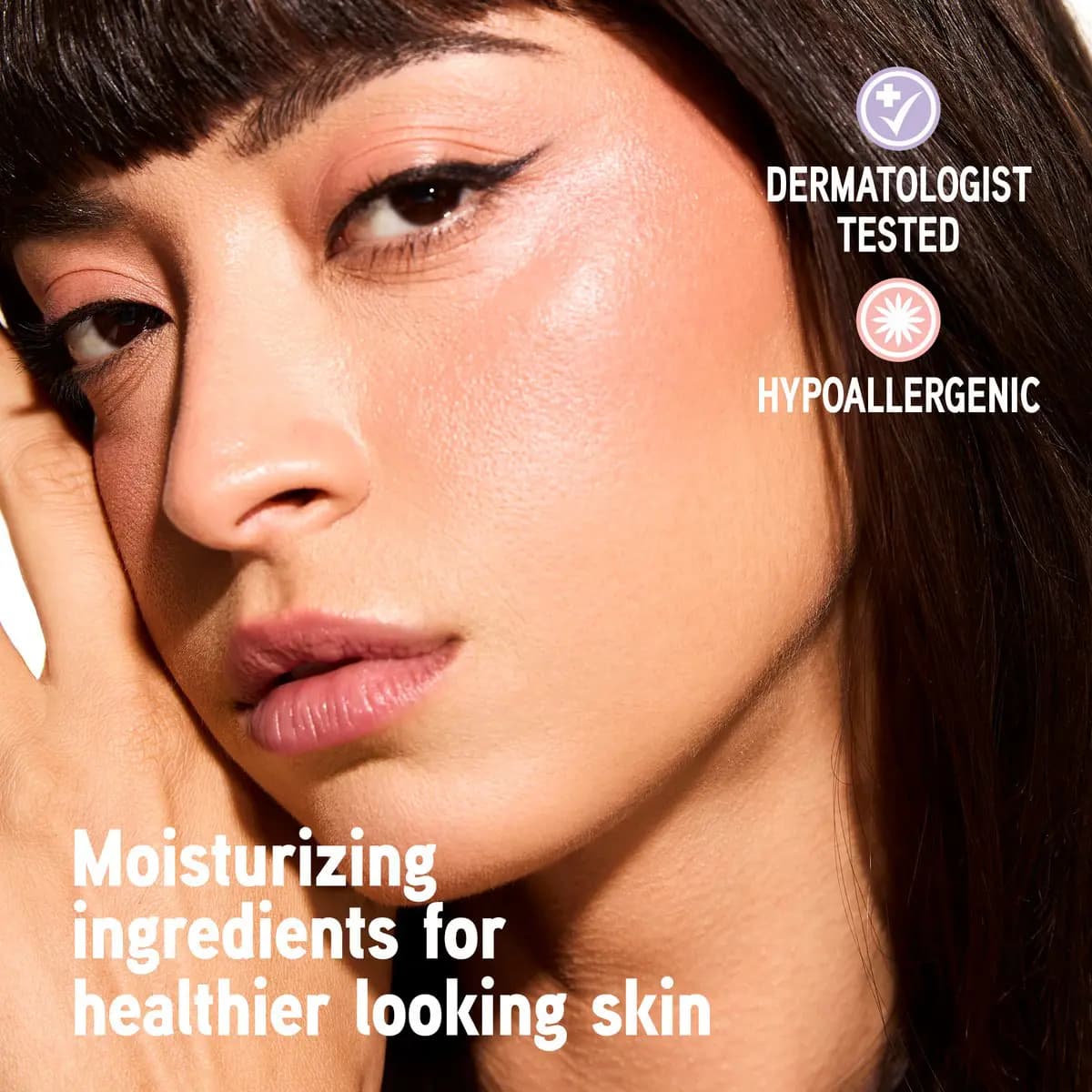 Close-up of brunette model with bangs wearing peachy blush, dermatologist tested and hypoallergenic badges beside her