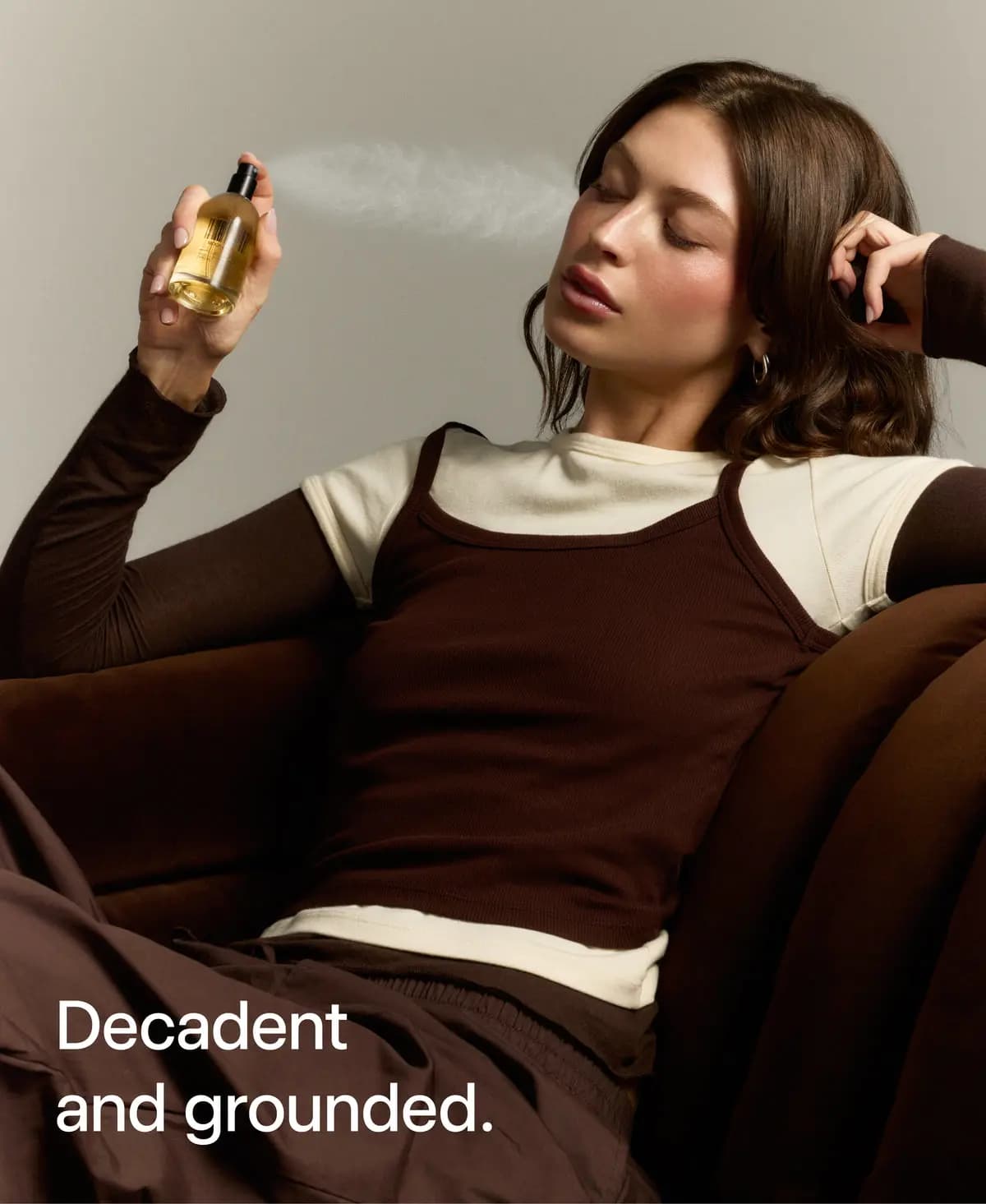 Brunette model in brown and cream layered top spraying DedCool perfume, text reads Decadent and grounded