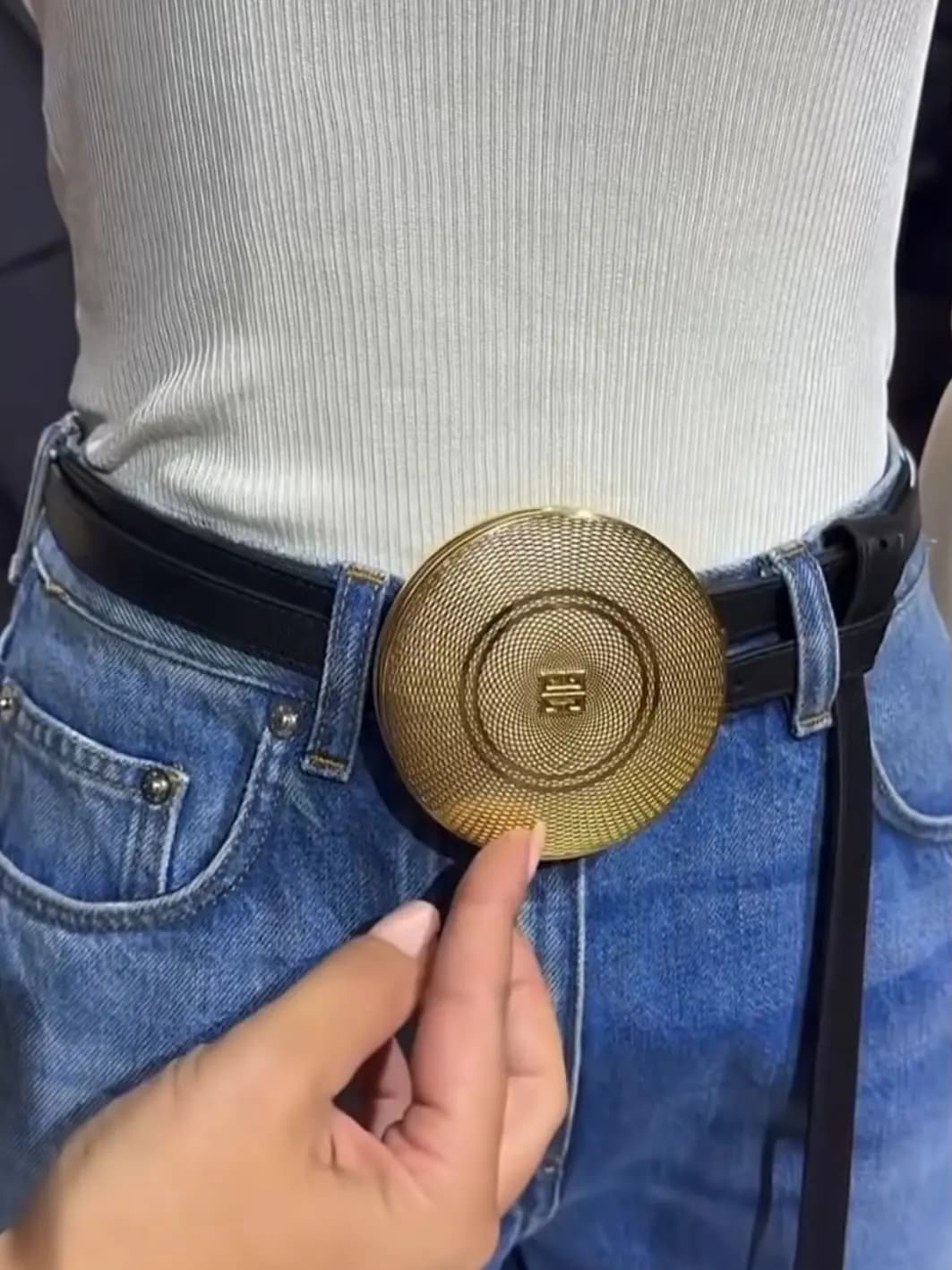 Closed gold compact buckle with guilloché engraving and a 4G logo, worn on a black belt over blue jeans
