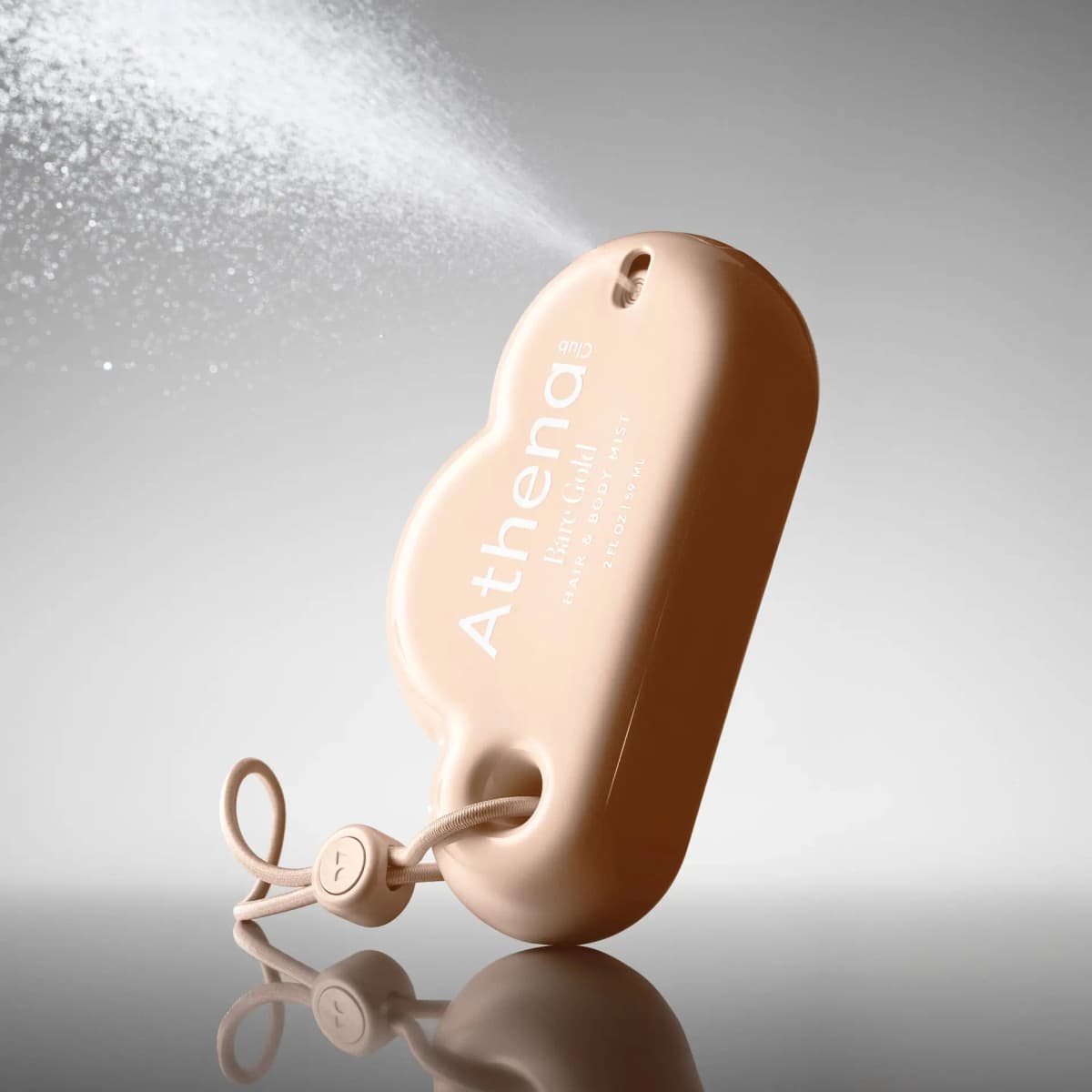 Cloud-shaped Bare Gold mini mist with an elastic cord loop spraying a fine shimmering mist on a grey backdrop
