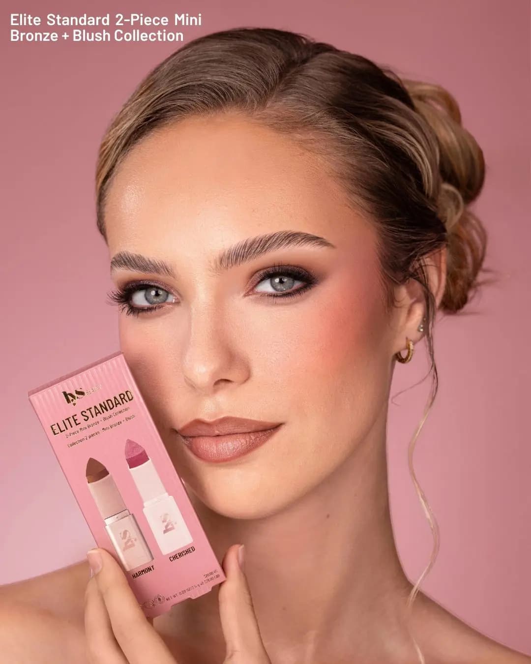 Model with rosy cheeks and a smoky eye holds the Elite Standard mini bronze and blush box in Harmony and Cherished