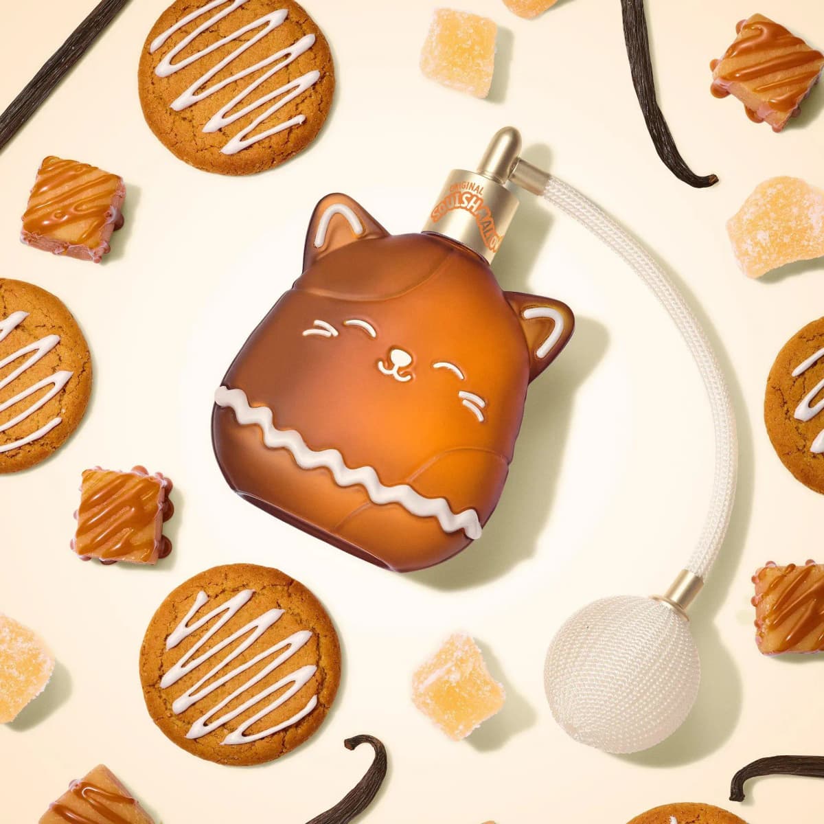 Amber cat-shaped perfume bottle on cream surface among iced ginger cookies, caramel squares, sugared jellies and vanilla pods