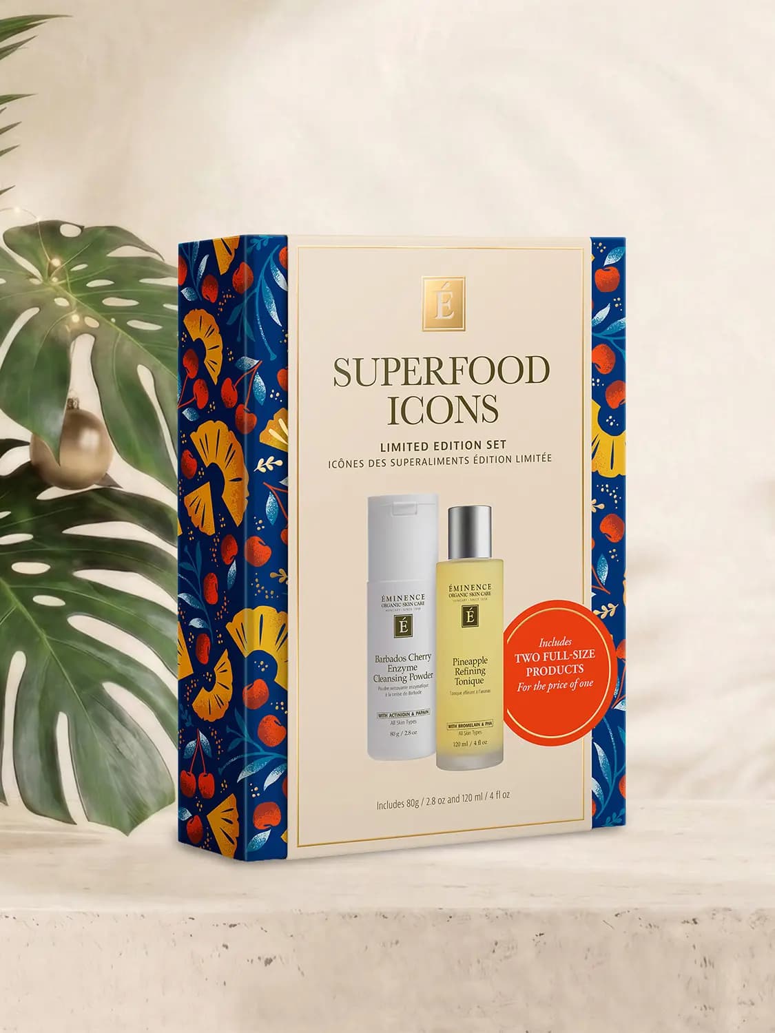Navy Superfood Icons box with orange pineapple and red cherry print, standing beside a monstera leaf on cream stone