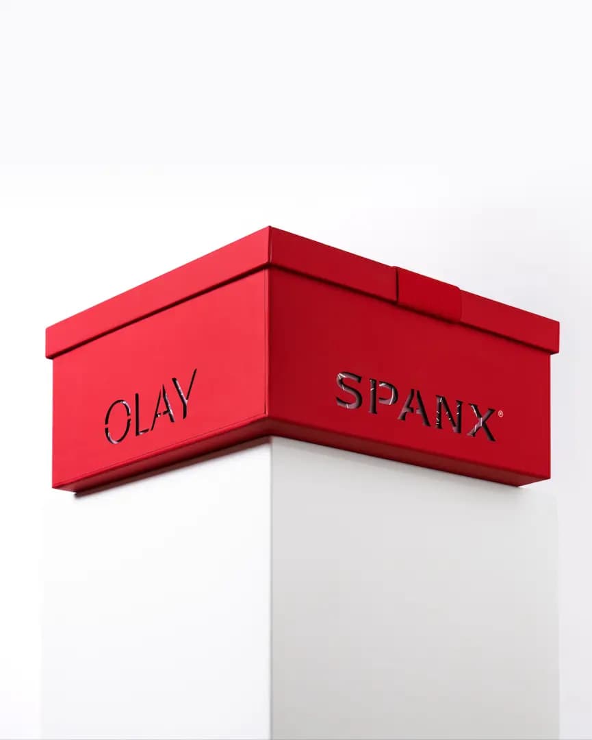 Red Spanx x OLAY collectible box with cut-out OLAY and SPANX lettering, displayed on a white pedestal