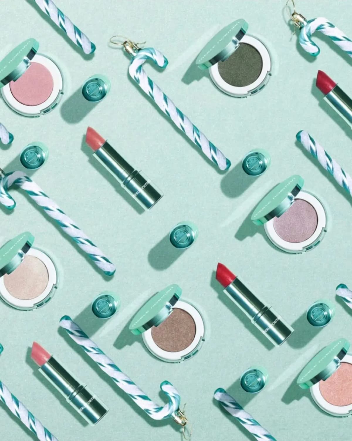 Merle Norman Glimmer Minted Holiday Collection lipsticks and eye shadows laid out with mint candy canes on a mint background