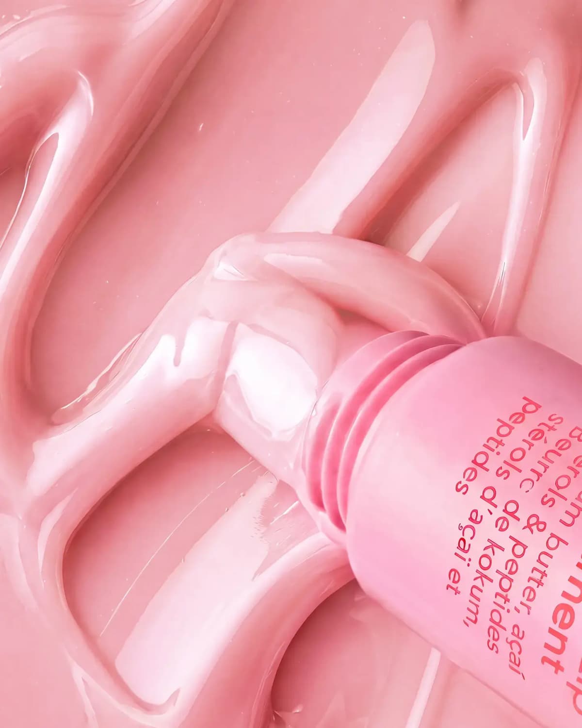 Close-up of glossy pale pink lip treatment swirled around the open nozzle of a pink tube