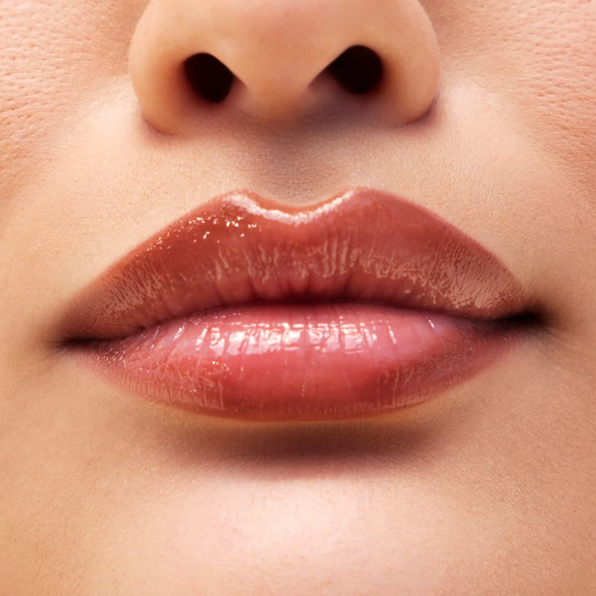 Close-up of lips wearing a high-shine sheer amber-rose gloss with a subtle shimmer