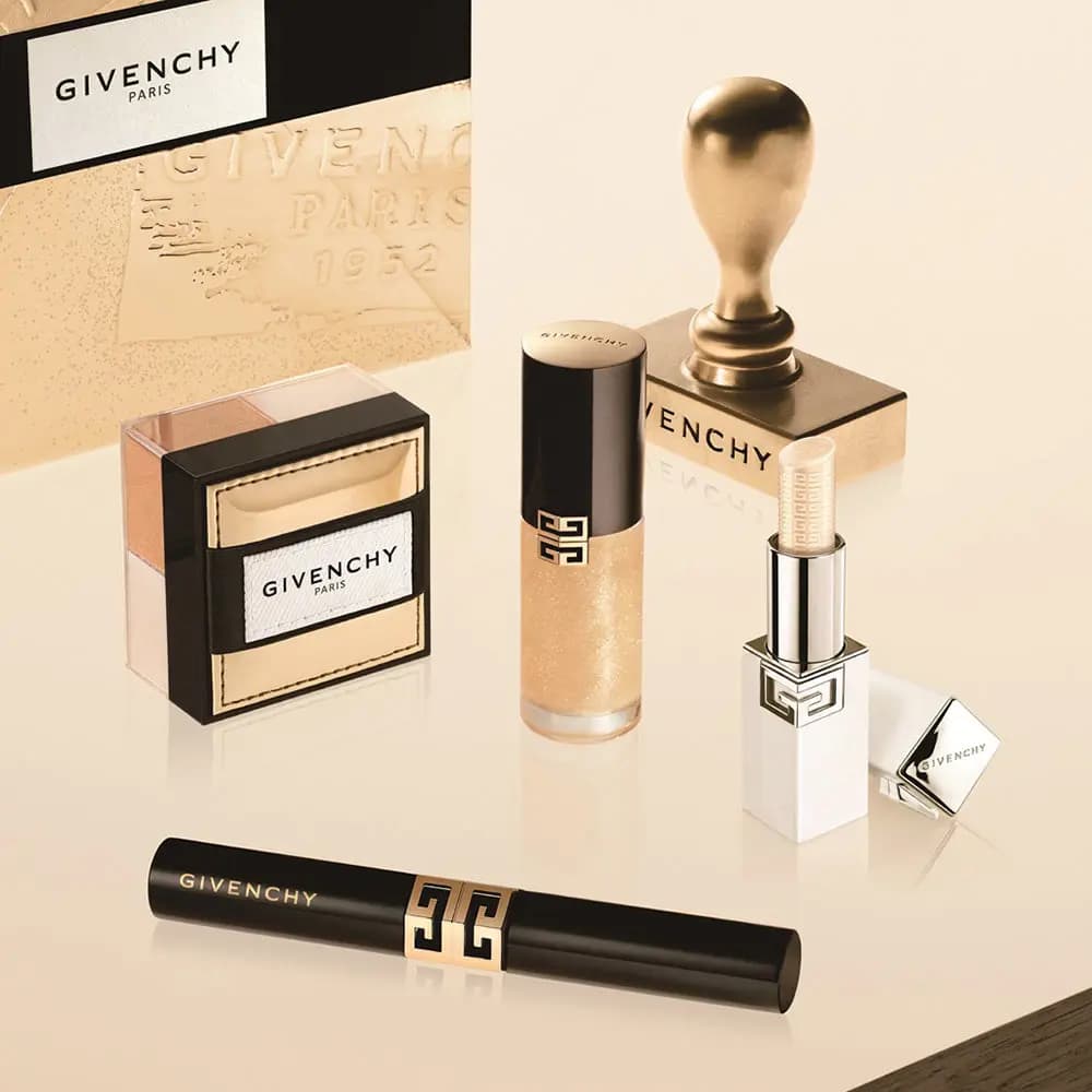 Holiday collection display: highlighter jar, gold lip oil, white lip balm and black lipstick beside a gold wax seal stamp