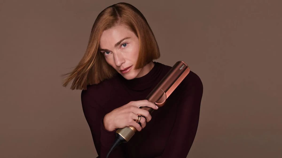 Model with a sleek copper bob in a burgundy turtleneck holding a copper and brass hair straightener