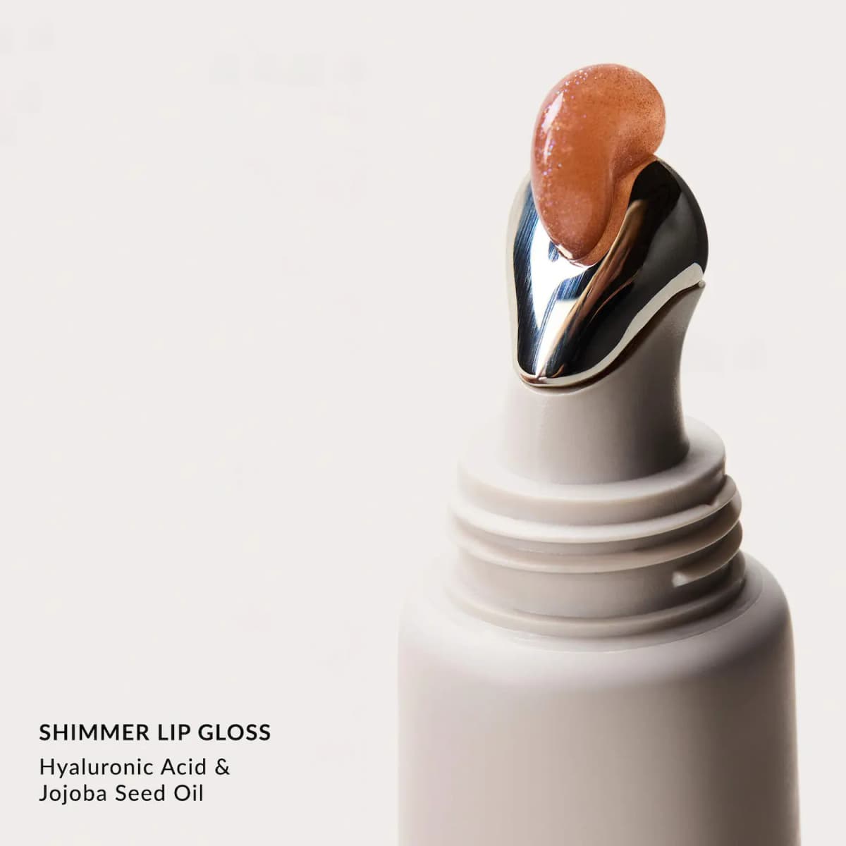 Metal applicator tip of a white tube topped with a drop of peachy bronze shimmer lip gloss