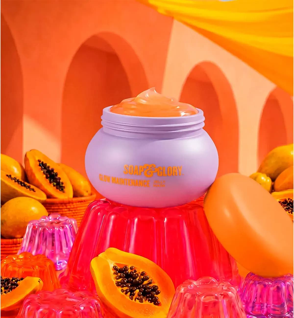 Lilac Glow Maintenance Jelly Mask jar with orange gel on a red jelly mould beside halved papayas