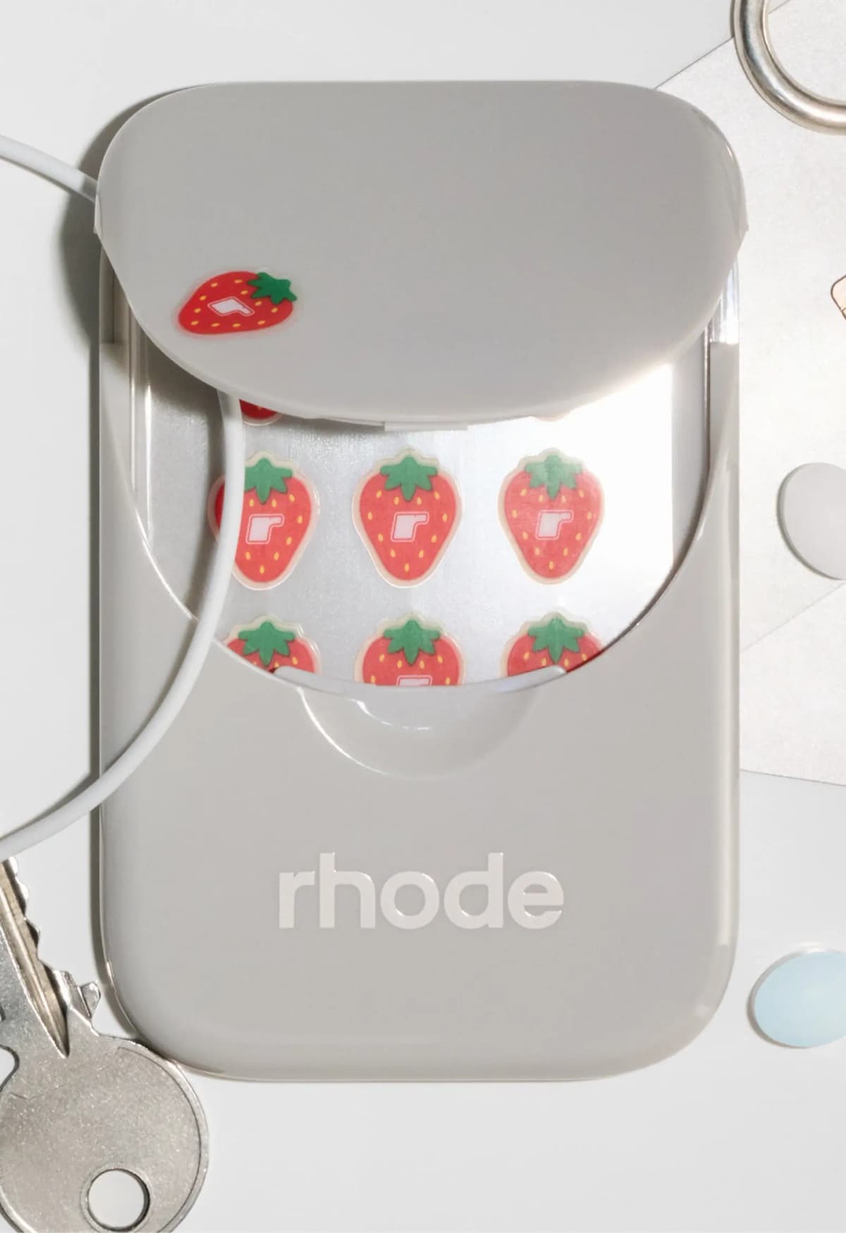 Grey case with lid partly open showing strawberry stickers, a sticker on the lid, beside keys and a white cable
