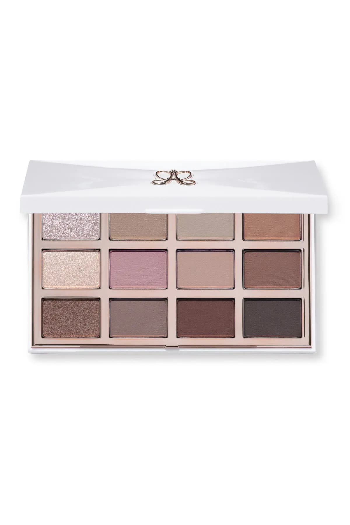 Closed white eyeshadow palette with rose-gold bow logo, open to reveal 12 shades in neutral, mauve and shimmer tones.
