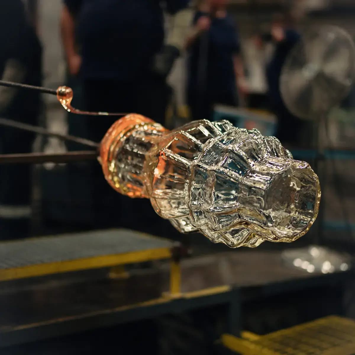 Molten rippled glass piece glowing orange on a blowpipe during mouth-blowing in a glass studio