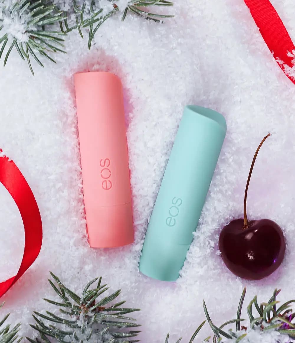 Pink and mint eos lip balm sticks nestled in fake snow with a dark cherry, red ribbon and pine sprigs