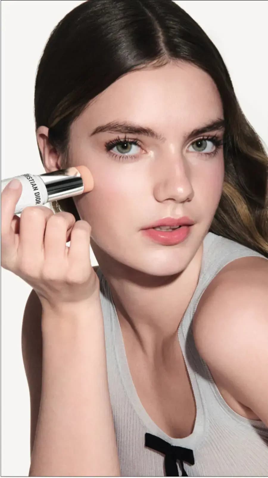 Model with slicked-back brunette hair and green eyes applies the stick to her cheek