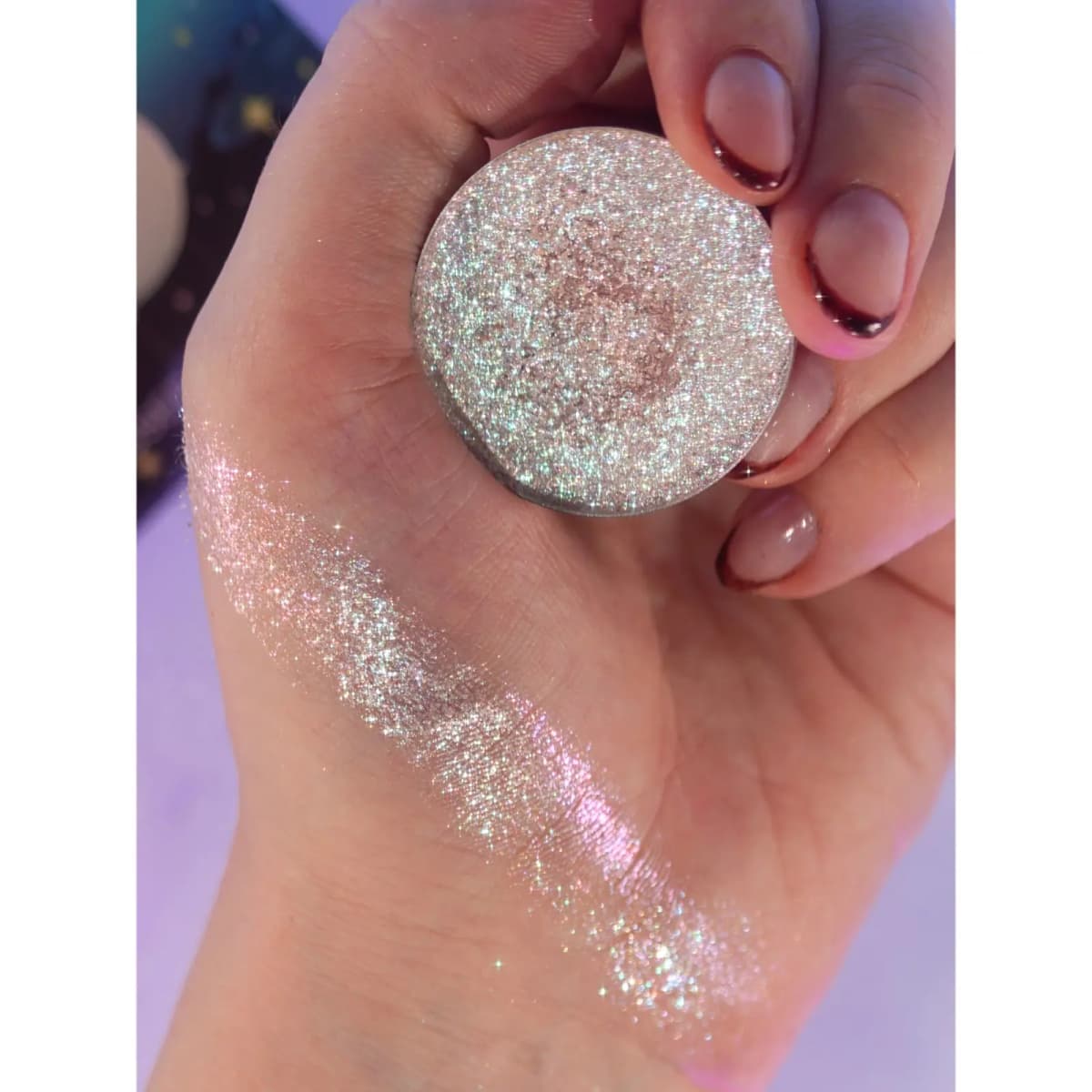 Hand holding a glittering silver pressed pan beside a sparkly pink-silver swatch across the back of the hand