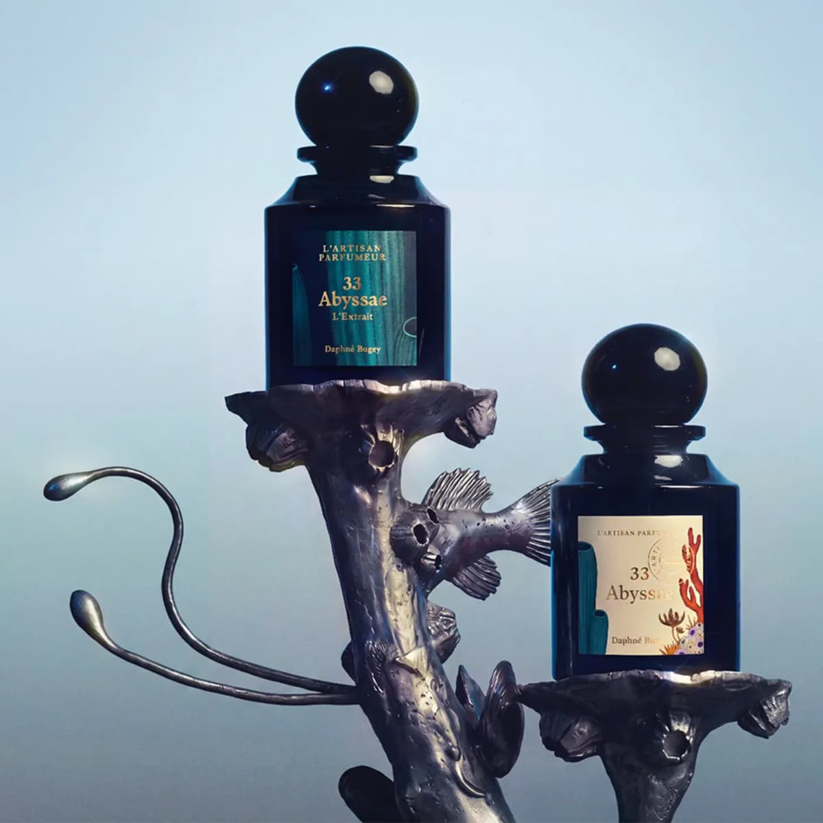Abyssae L'Extrait and the cream-labelled Abyssae Eau de Parfum on silver coral-like stands against a pale blue sky