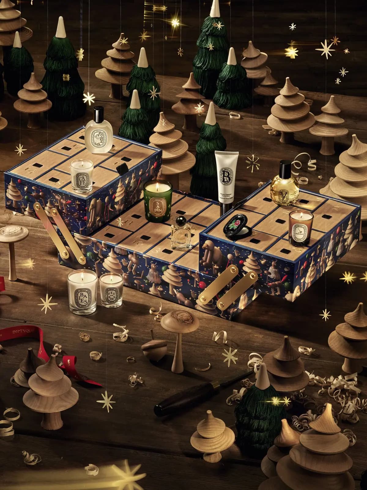 Diptyque Advent Calendar 2026 opened as a tiered toolbox with Sapin, Café and Baies candles amid wooden trees and gold stars