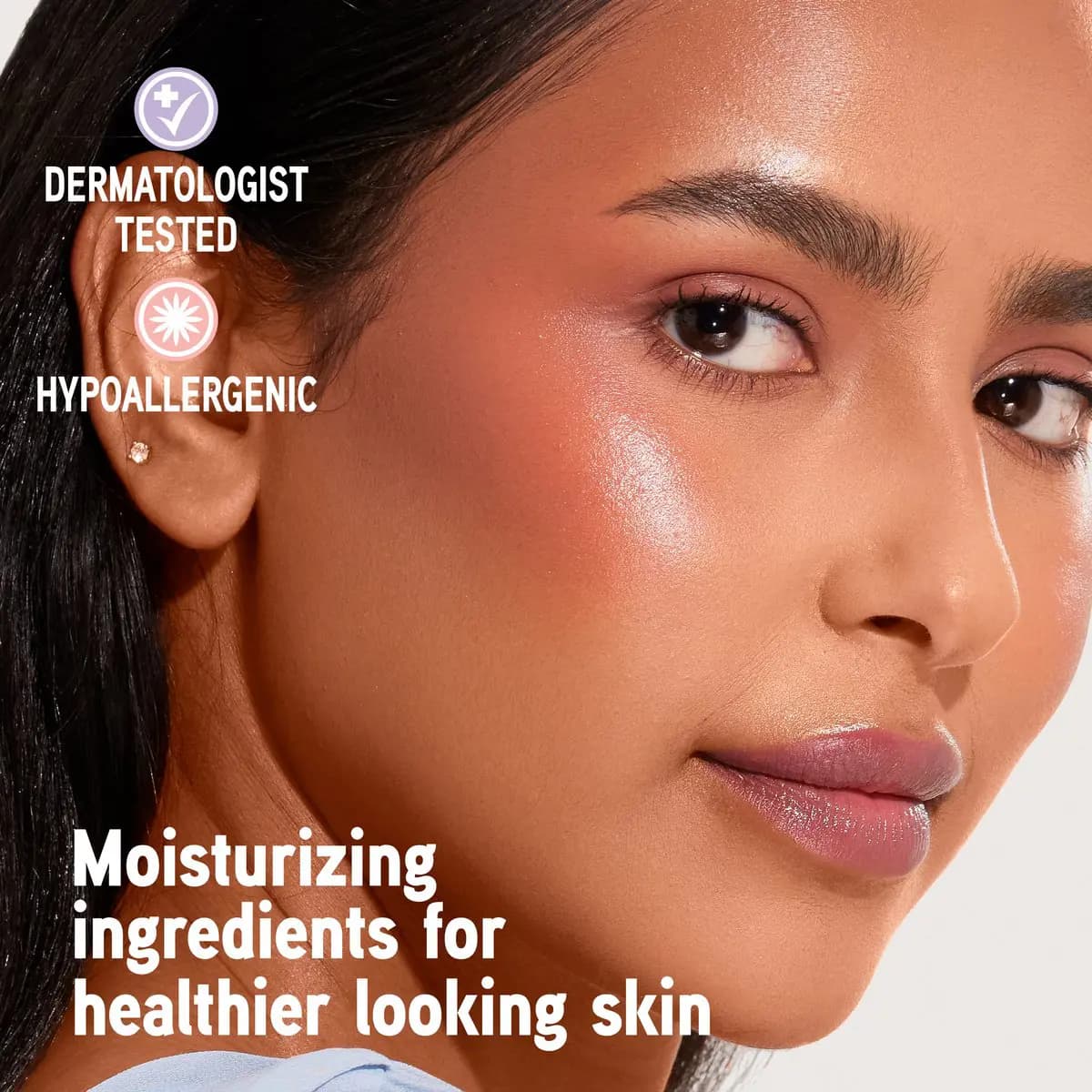 Medium-toned model with glowy peach blush on cheekbone, dermatologist and hypoallergenic badges on left