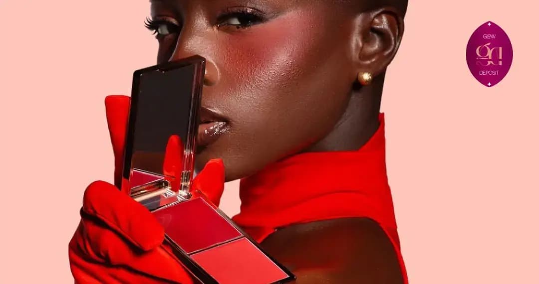 Model in red gloves and top holds a red blush compact to her face, showing a vivid red flush on her cheek