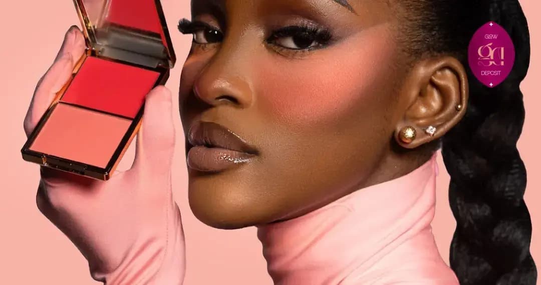 Model with deep skin in a pink turtleneck and gloves holds a red and coral blush duo, wearing soft rosy blush