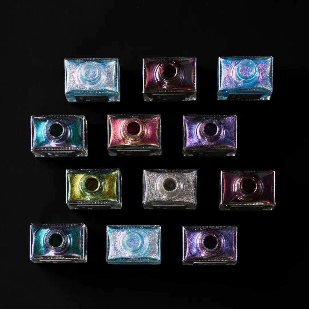 Overhead view of eleven square polish bottles in rows showing aqua, pink, violet, green, silver and red shifting colours