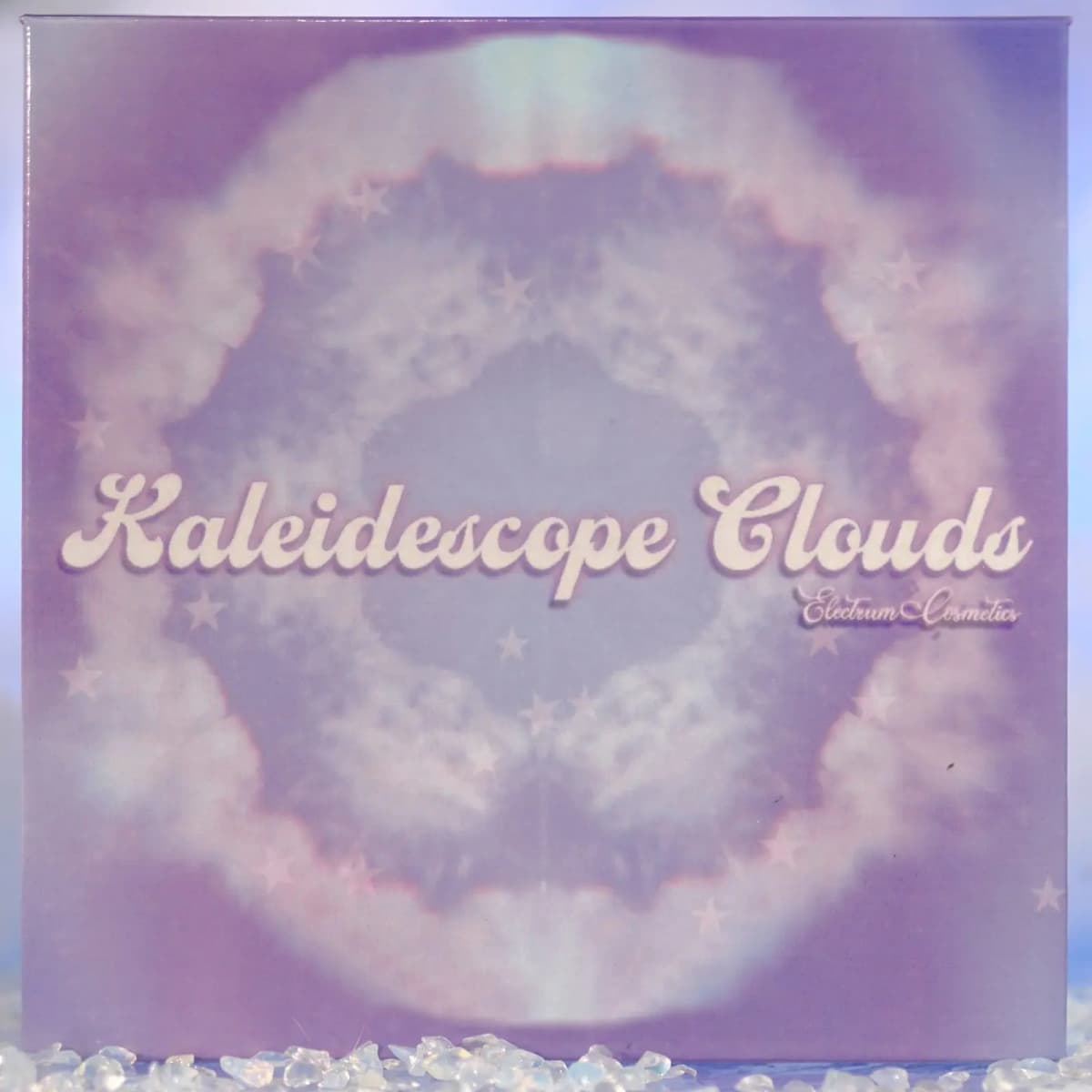 Lilac palette box with a kaleidoscopic cloud and star pattern and script title, set on opalescent crystal chips