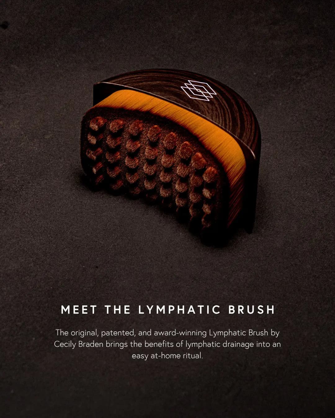 Half-moon Lymphatic Brush with dark wood-grain top, white geometric logo, amber fibres and brown nubs on a dark backdrop