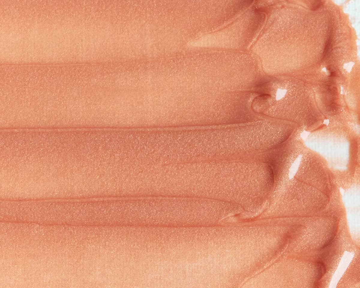 Creamy peachy-champagne balm swatched in smooth glossy streaks with fine shimmer