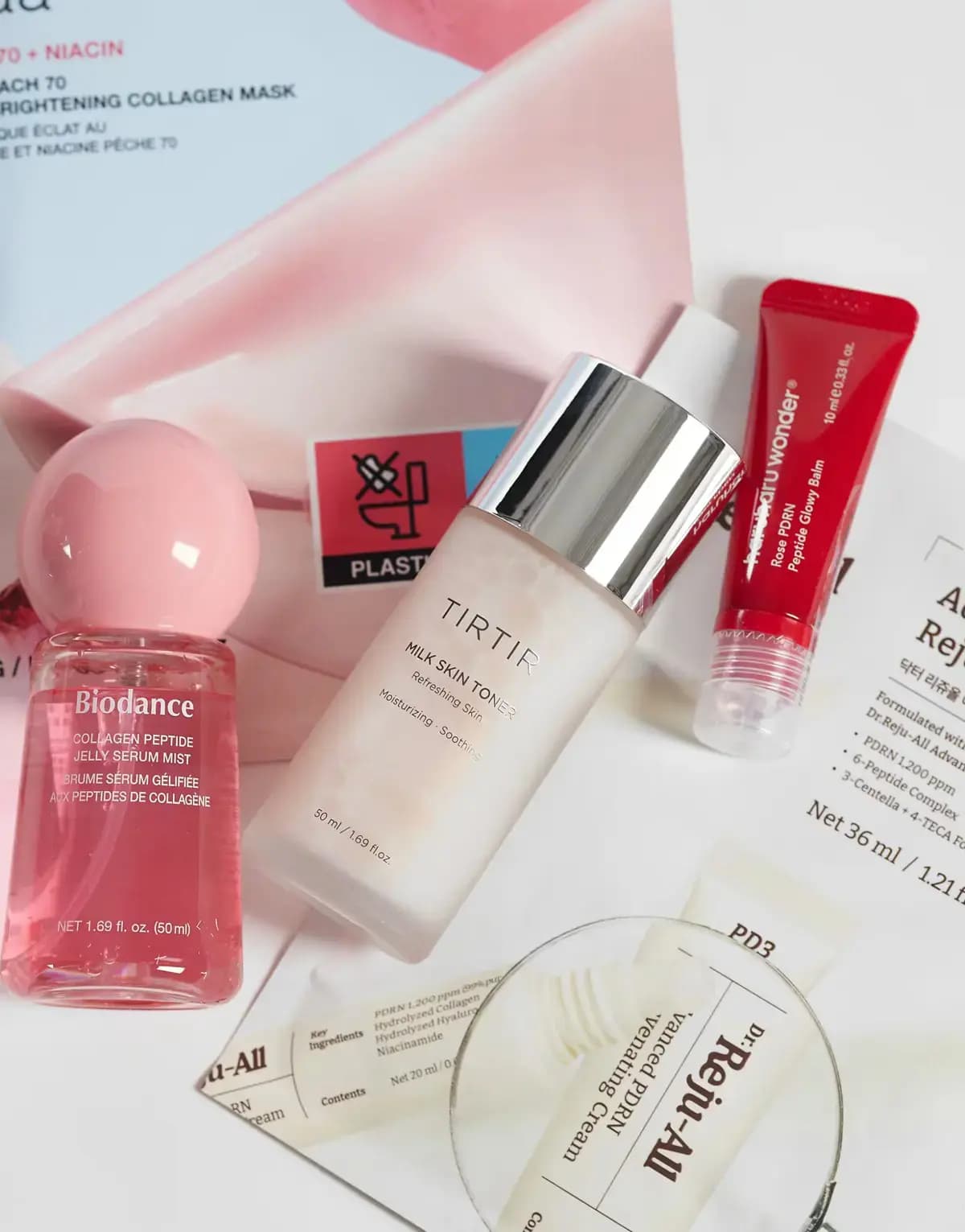 Flat lay of pink Biodance mist, frosted TIRTIR Milk Skin Toner, red haruharu wonder tube and Dr.Reju-All mask packets