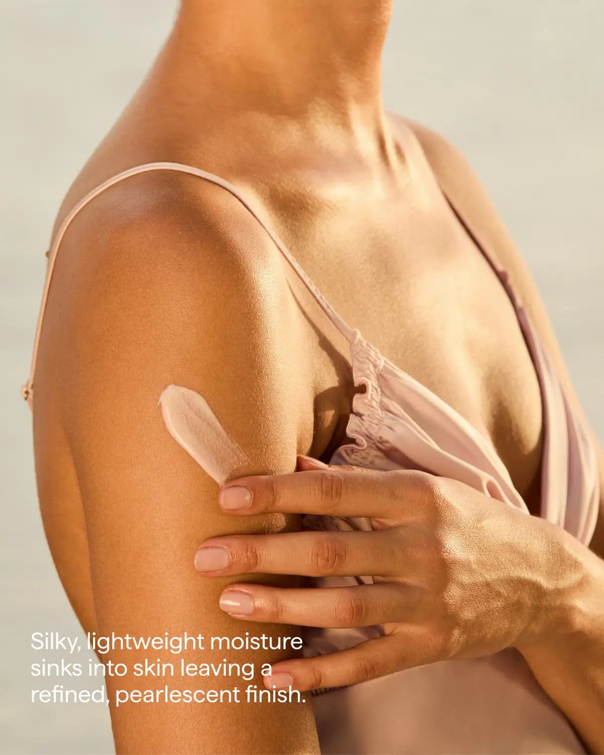 Hand spreading a stripe of pink lotion on a sunlit upper arm, captioned about a pearlescent finish
