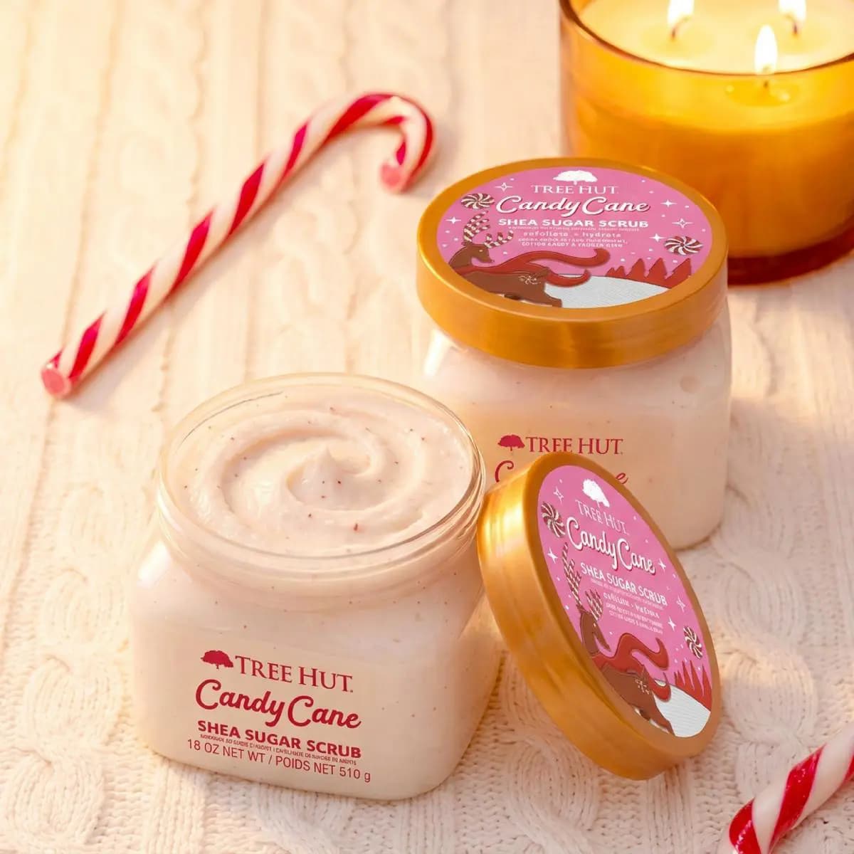 Two Candy Cane Shea Sugar Scrub jars with creamy white scrub, a candy cane, and a glowing candle on cable-knit background