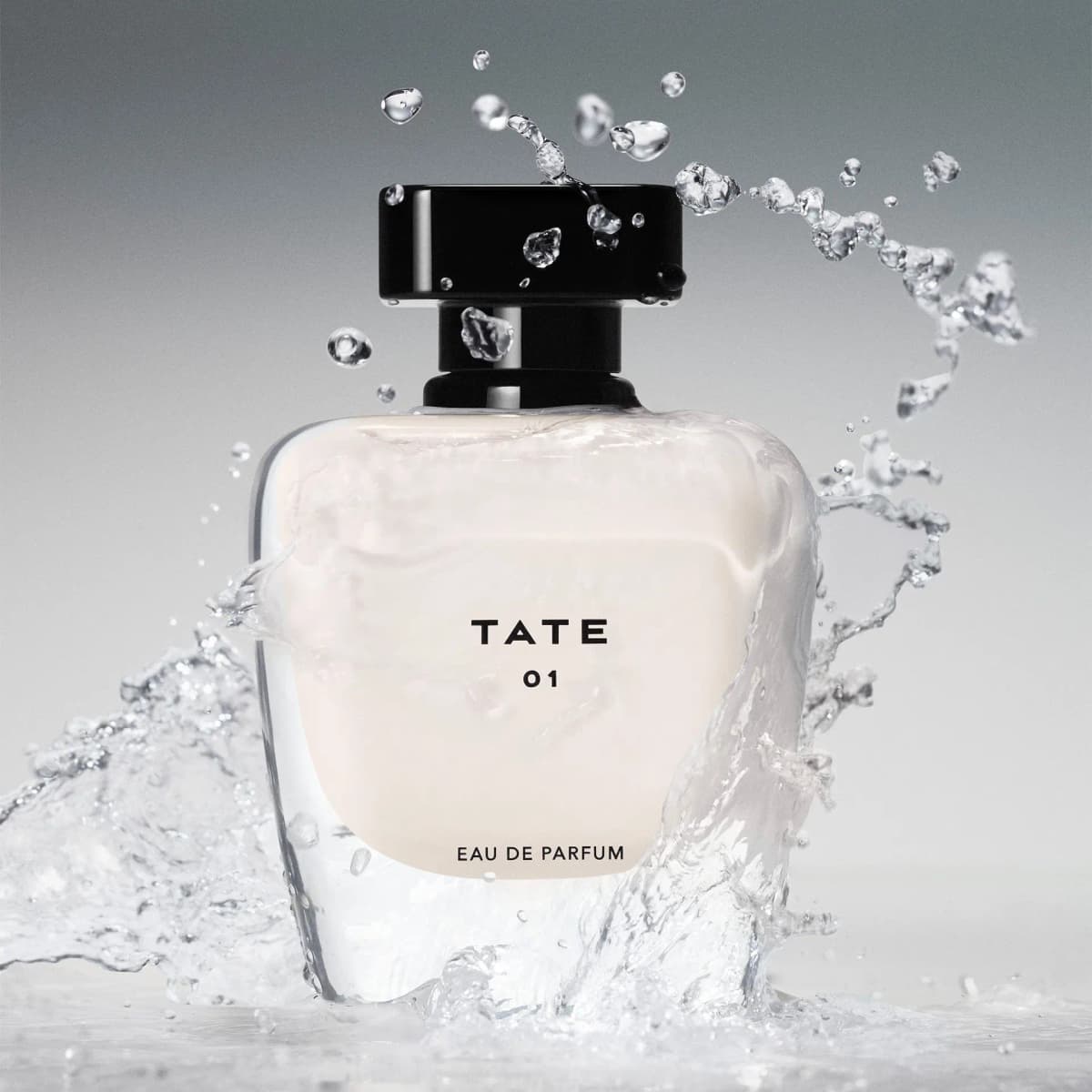 TATE 01 Eau de Parfum bottle with cream glass and glossy black cap, surrounded by splashing water on a grey backdrop