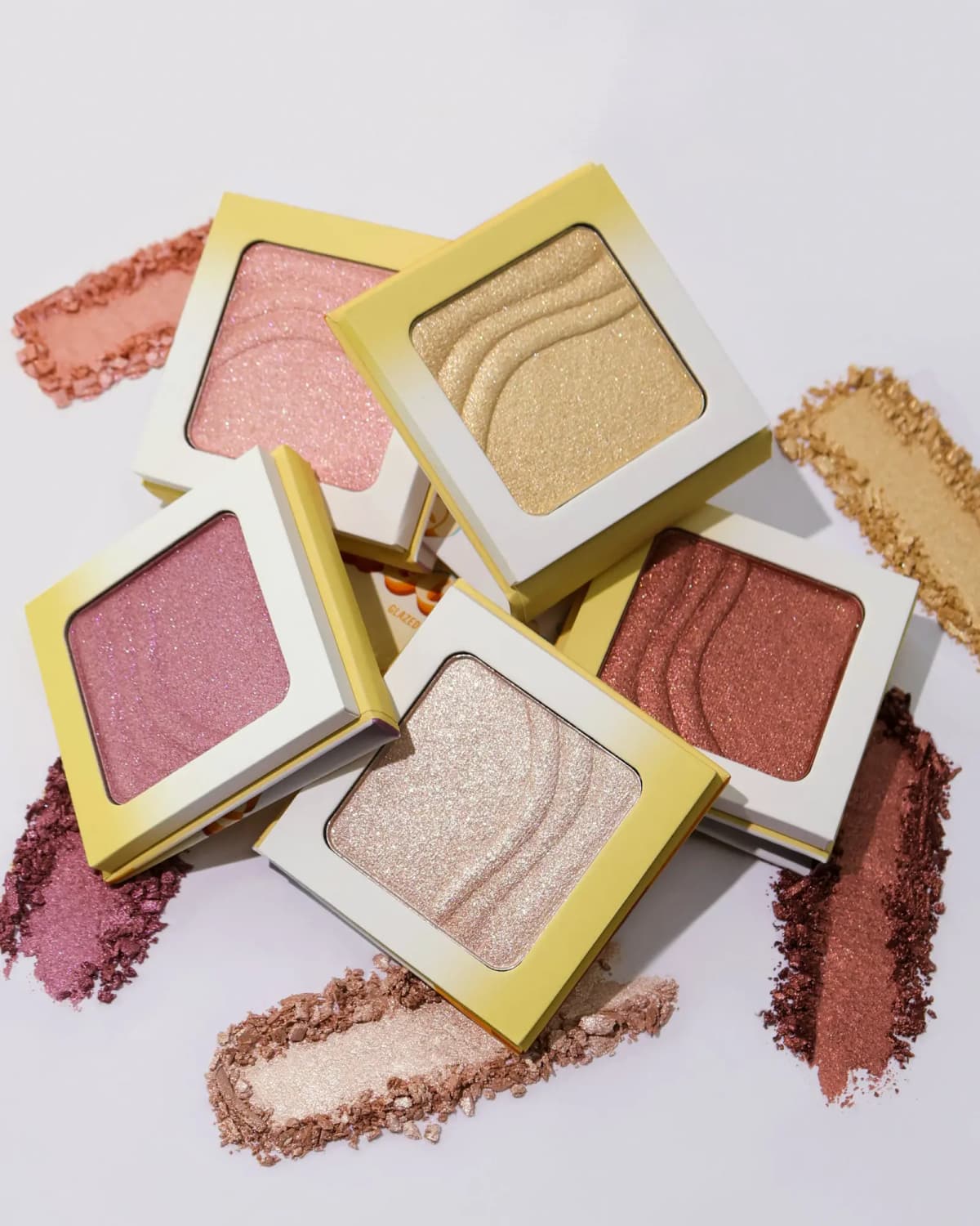Stacked open highlighter compacts in pink, gold, mauve, bronze, and pearl surrounded by powder swatches