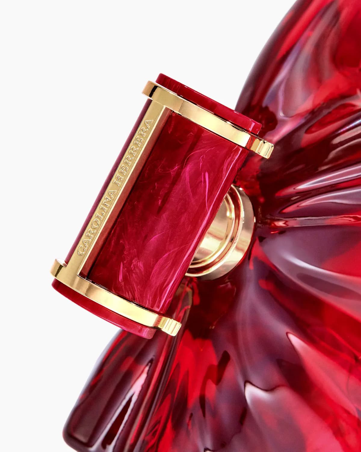 Close-up of the marbled red cap with gold frame engraved Carolina Herrera against rippled red glass