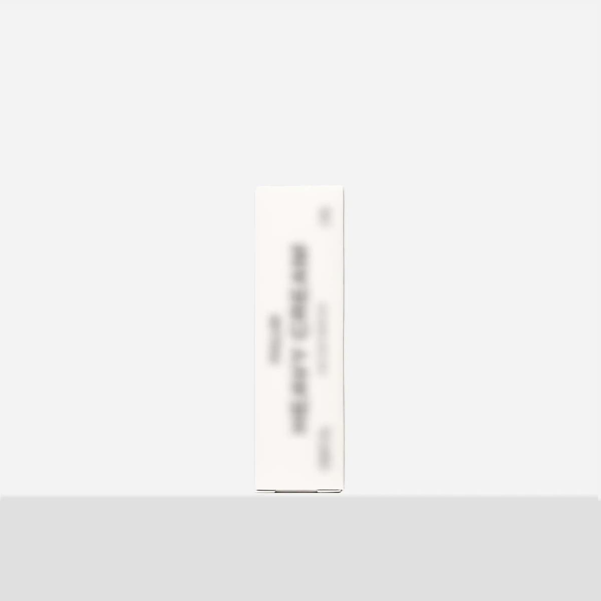 Slim white box with blurred-out text standing upright on a light grey surface against a plain white background