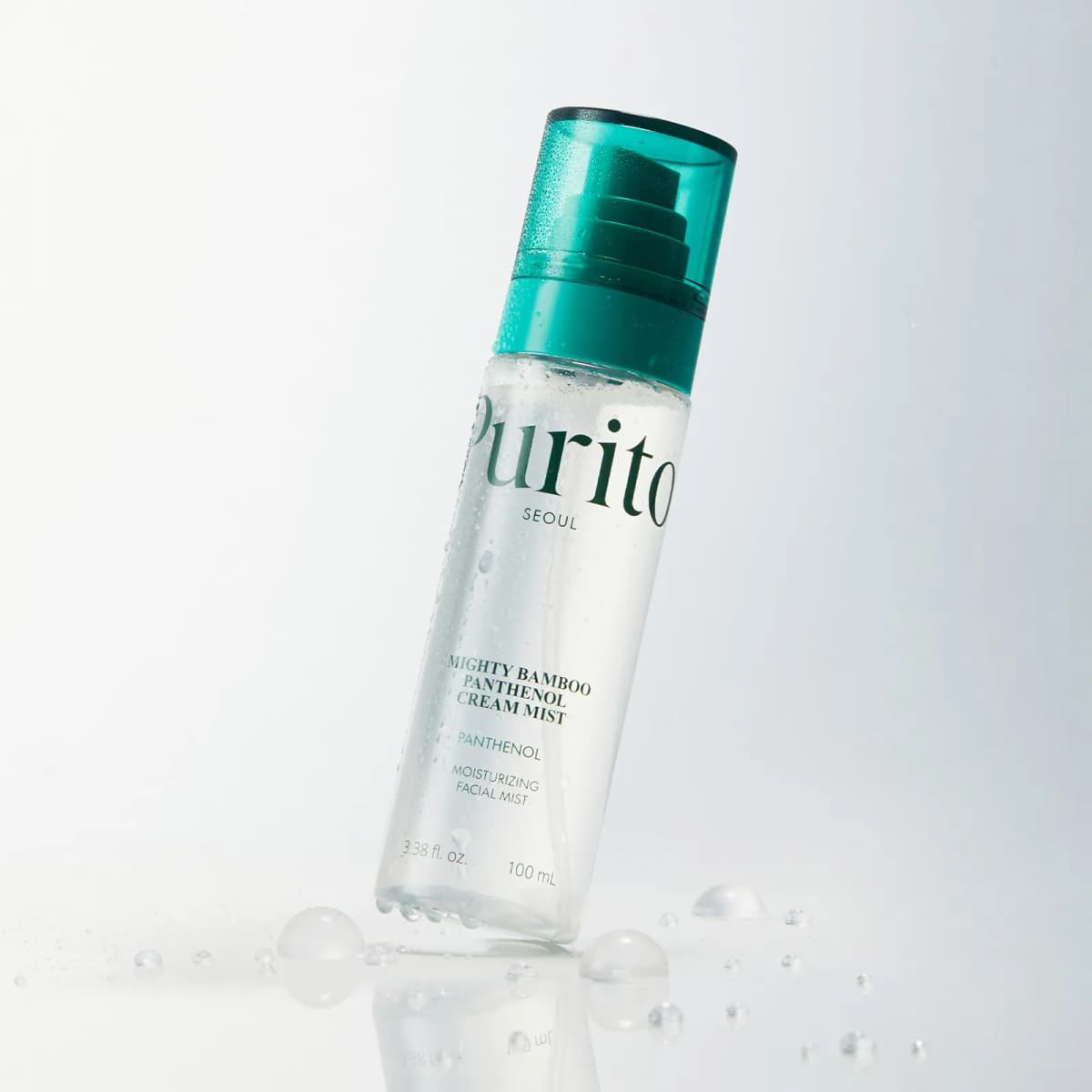Dewy Mighty Bamboo Panthenol Cream Mist bottle with teal cap tilted on a white surface among water droplets.